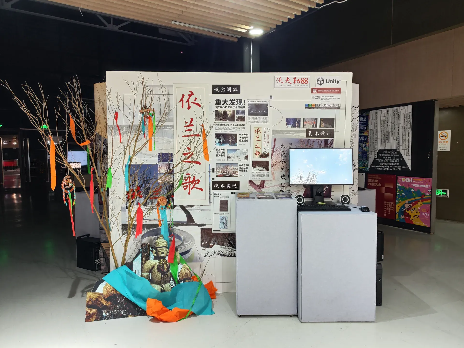 Exhibition booth with a game poster, a monitor and a decorated branch with colorful ribbons